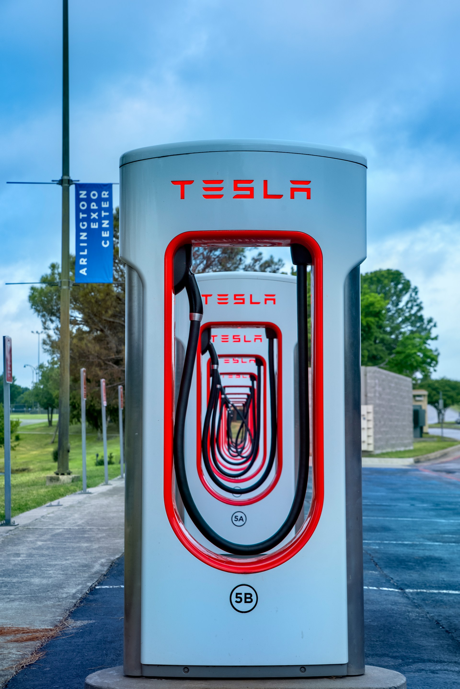 Tesla charging station with multiple charging units aligned in perspective, outdoor setting with blue sky and trees